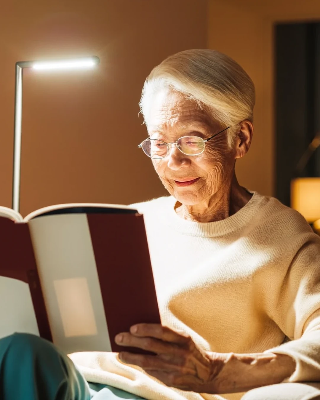 Signora anziana che legge un libro in poltrona la sera con una lampada da lettura orientata sulla pagina